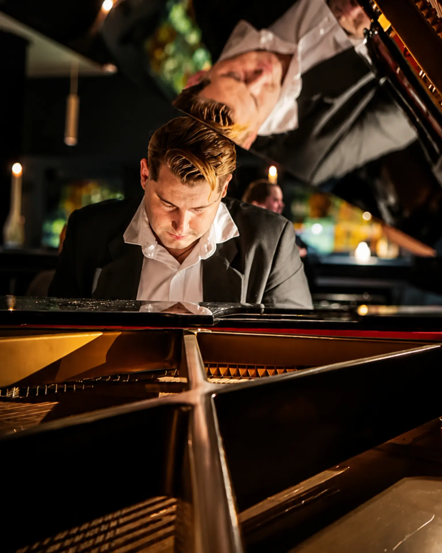 Tom Carvalho sorrindo ao piano de cauda durante uma apresentação