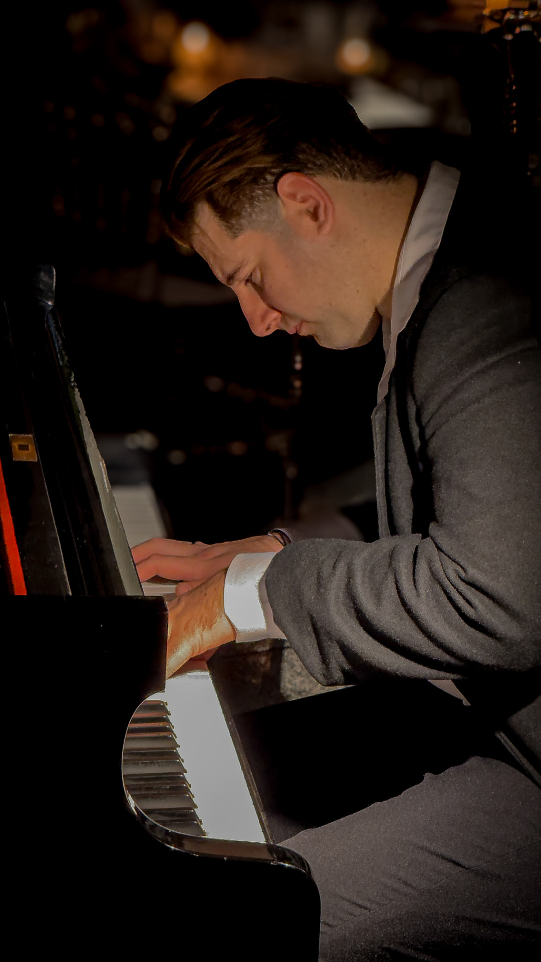 Tom Carvalho de perfil, com as mãos sobre o teclado do piano durante uma aula